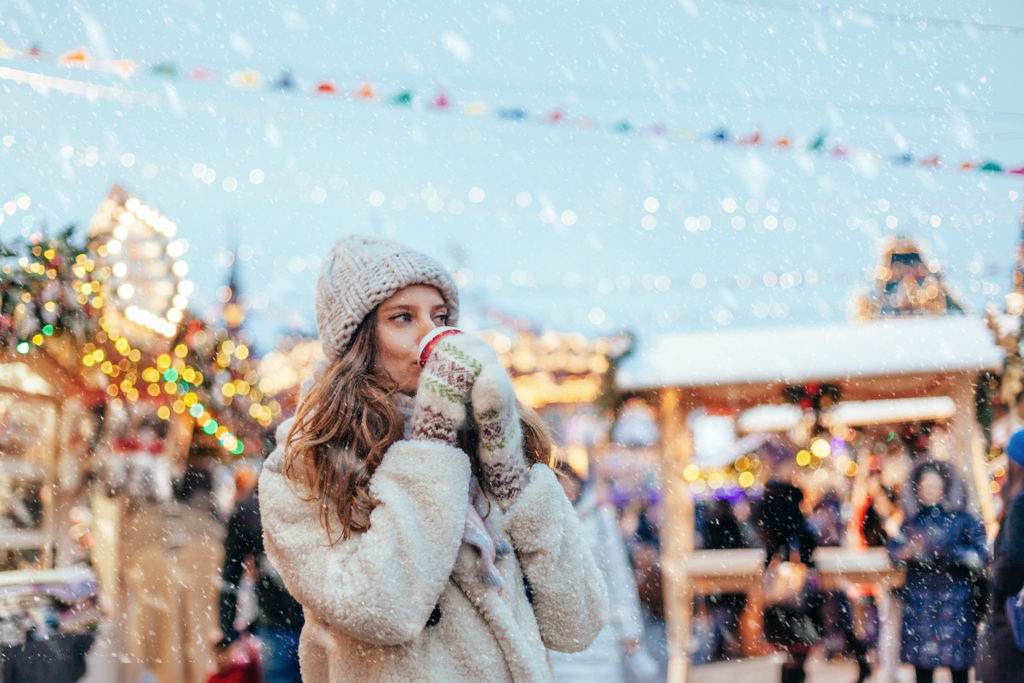 Woman drinking hot drink at a cold holiday festival in December.